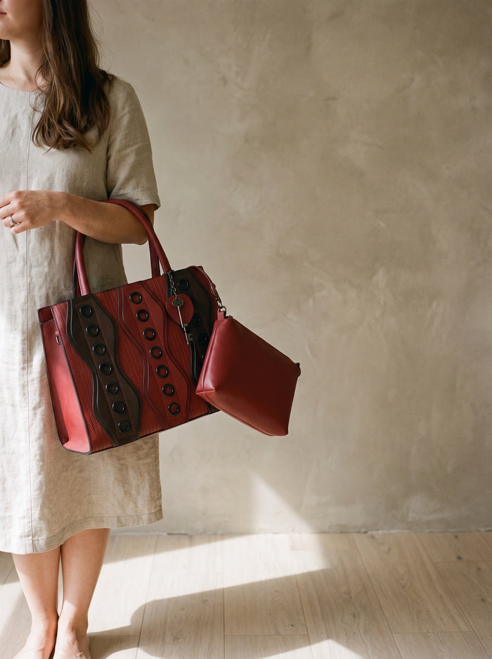 The Sutton Bag in Burgundy, held by the top handle at the hip