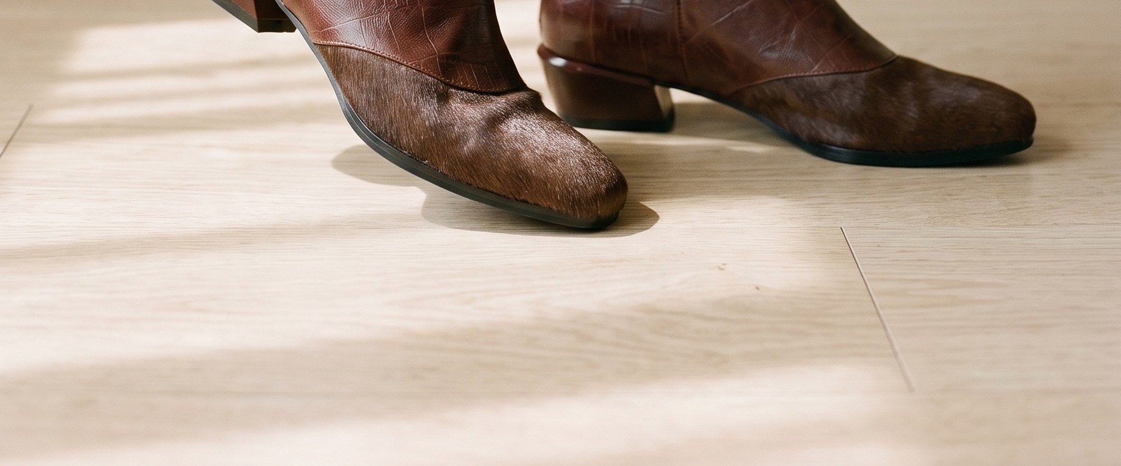 Brown leather ankle boots, worn on a pale oak floor